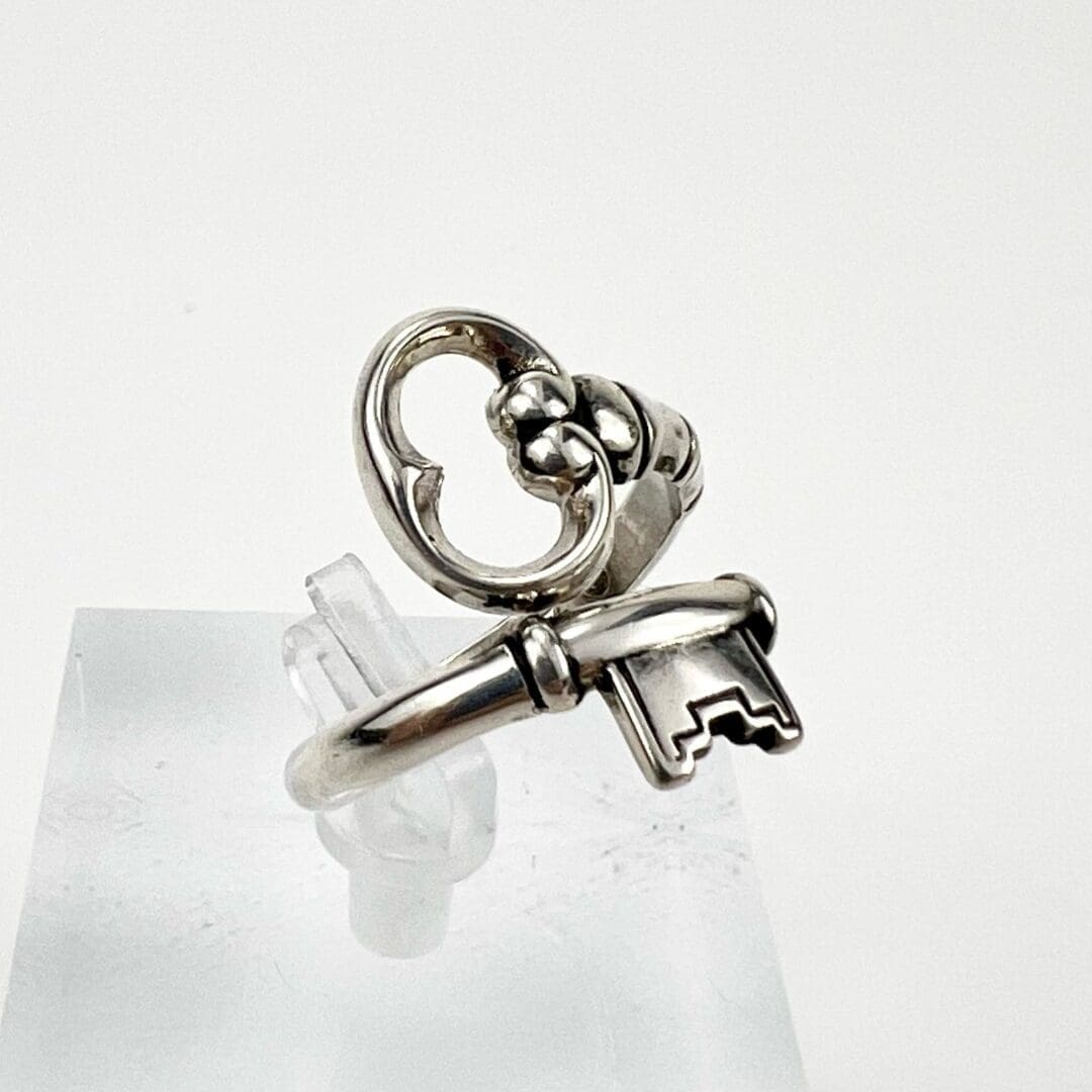 Silver ring with key design on stand.