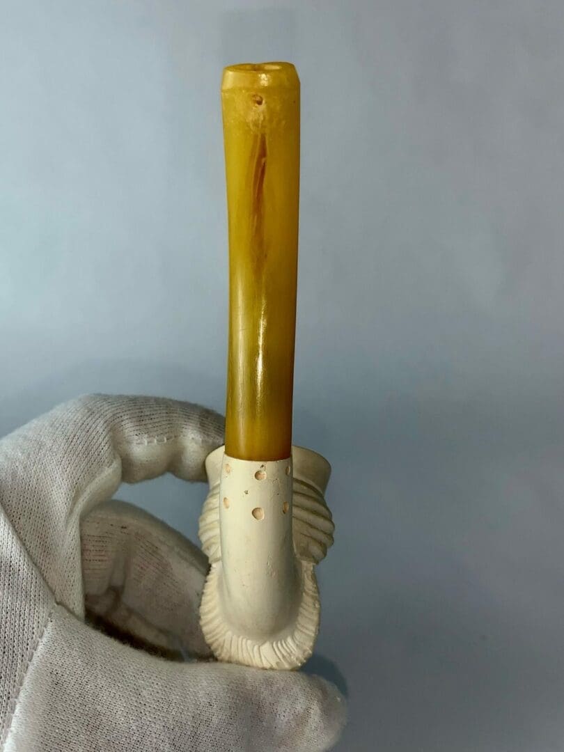 Carved pipe with amber-colored stem, held upright.