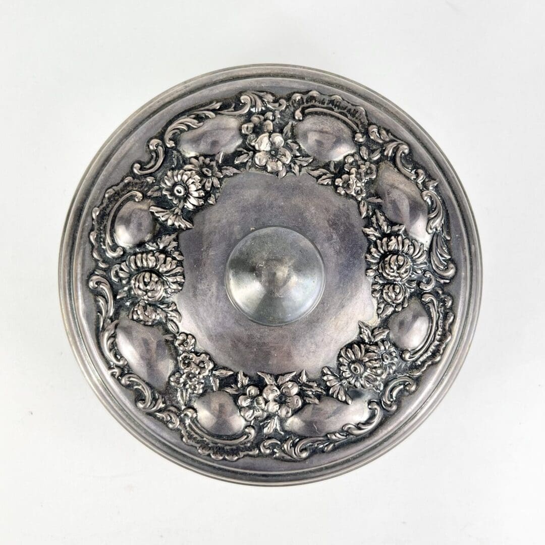 Ornate silver lid with floral decoration.
