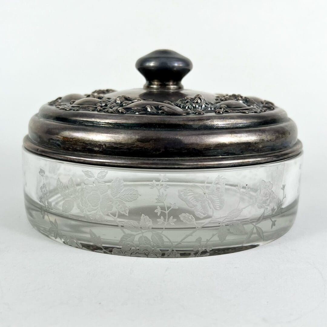 Glass jar with ornate metallic lid.
