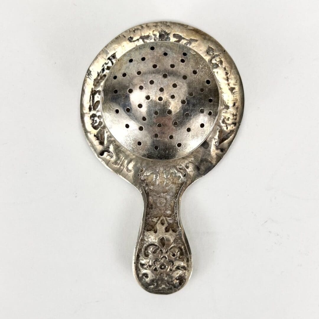 Ornate silver tea strainer with handle.