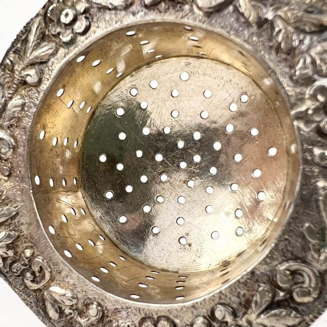 Ornate silver strainer with floral design.