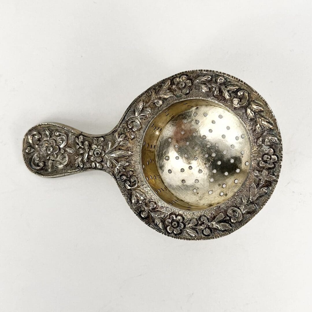 Ornate silver tea strainer with floral design.