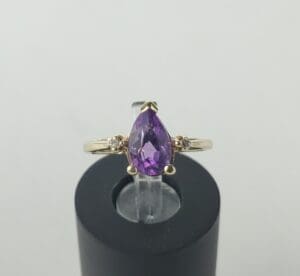 Gold ring with purple gemstone on stand.