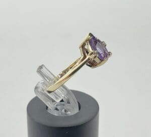 Gold ring with purple gemstone on stand.