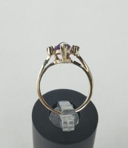 Gold ring with purple gemstone on stand.