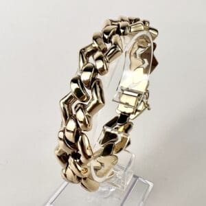 Gold bracelet on a transparent display stand.