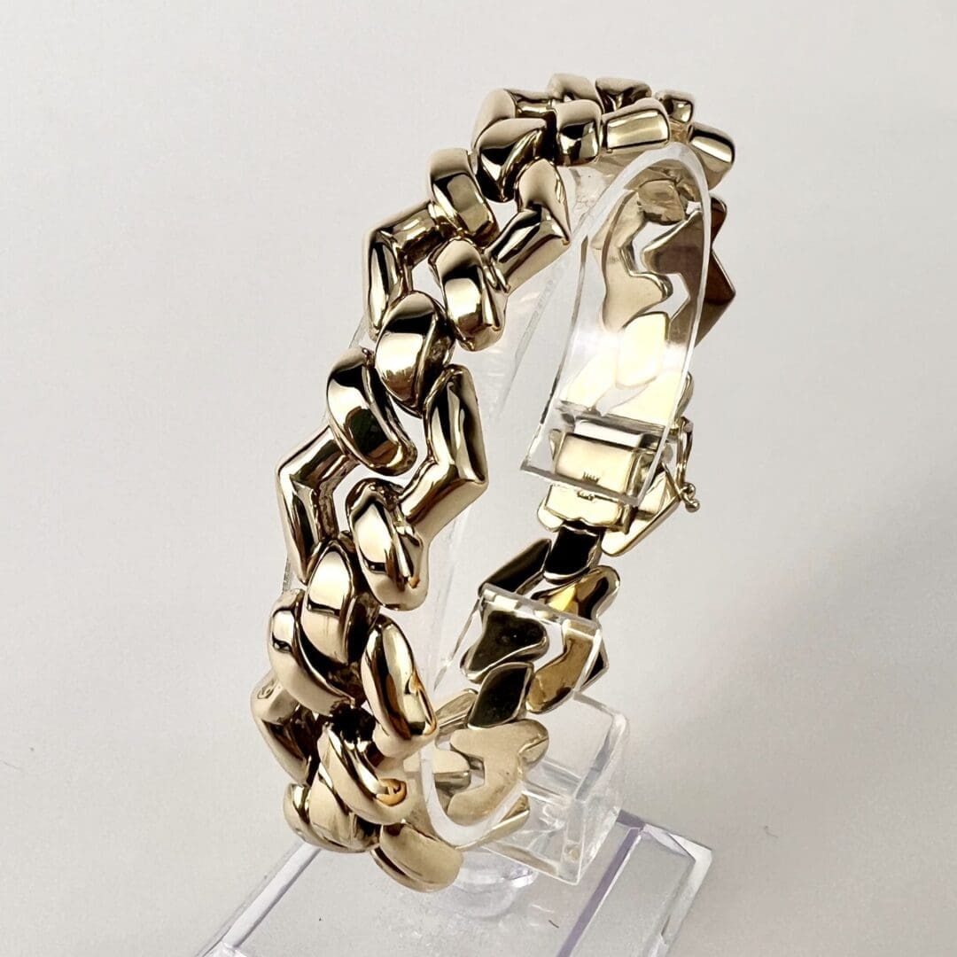 Gold bracelet on a transparent display stand.