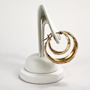Gold hoop earrings on white display stand.
