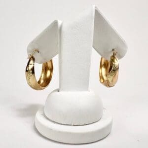 Gold hoop earrings on white display stand.