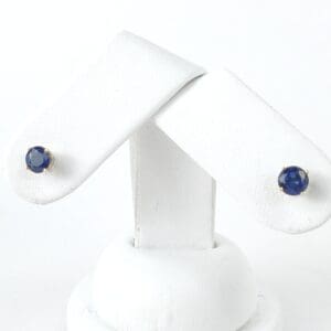 Blue gemstone stud earrings on white stand.