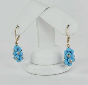 Blue beaded earrings on white display stand.