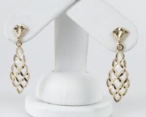 Gold drop earrings on white display stand.