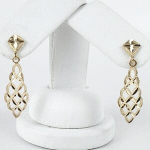 Gold lattice drop earrings on display stand.