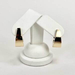 Gold earrings on white display stand.