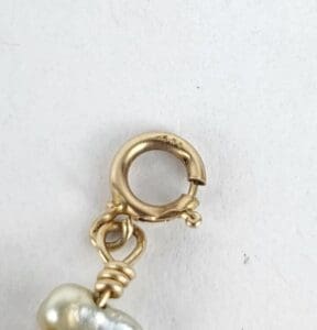 Gold jewelry clasp with attached pearl detail.