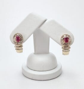 Gold earrings with red gemstones on stand.
