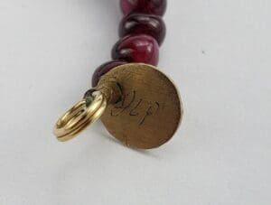 Gold tag with engraved initials, red beads.