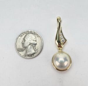 Gold pendant with pearl next to quarter.