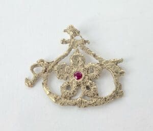 Ornate gold brooch with a red gem.