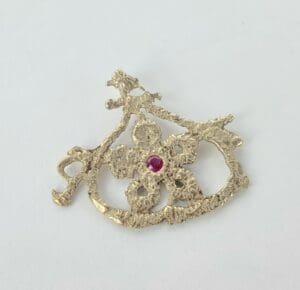 Gold pendant with floral design and gemstone.