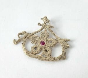 Ornate gold brooch with central red gem.