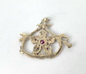 Gold pendant with red gemstone in center.
