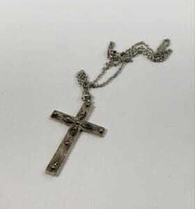Silver cross pendant with chain on display.