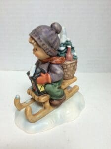 Child figurine sledding with basket and lantern.