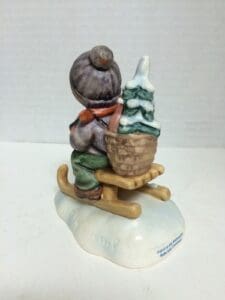 Child figurine on sled with tree.