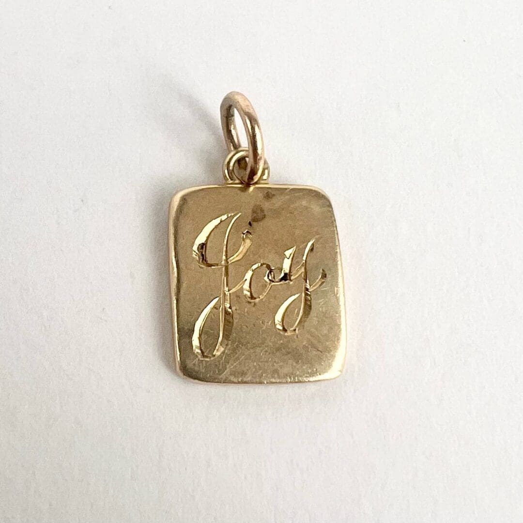 Gold pendant with "Joy" engraving.