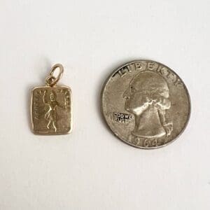 Gold pendant beside a 1964 quarter coin.