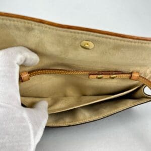 Gloved hand holding open beige purse.