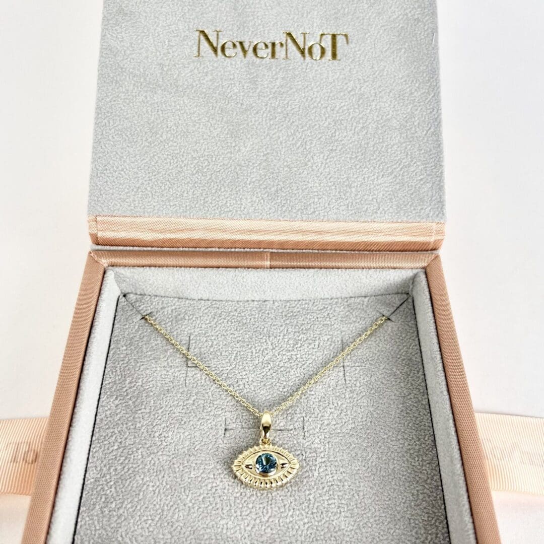 Gold necklace with blue gem in box.