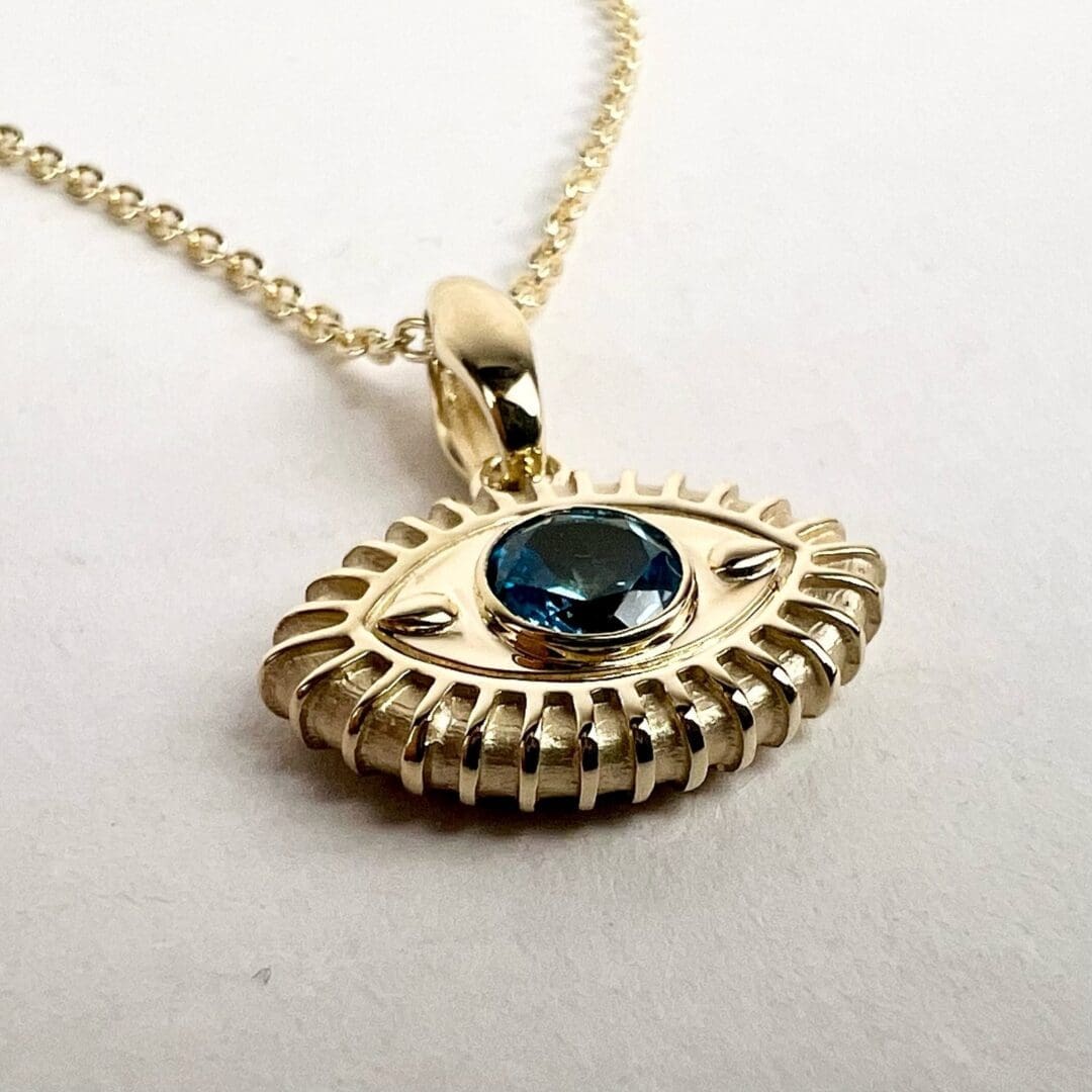 Gold eye pendant with blue gemstone.