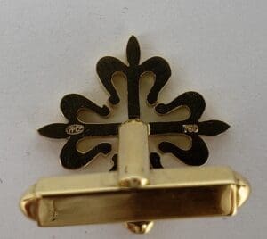 Gold pin with fleur-de-lis design.