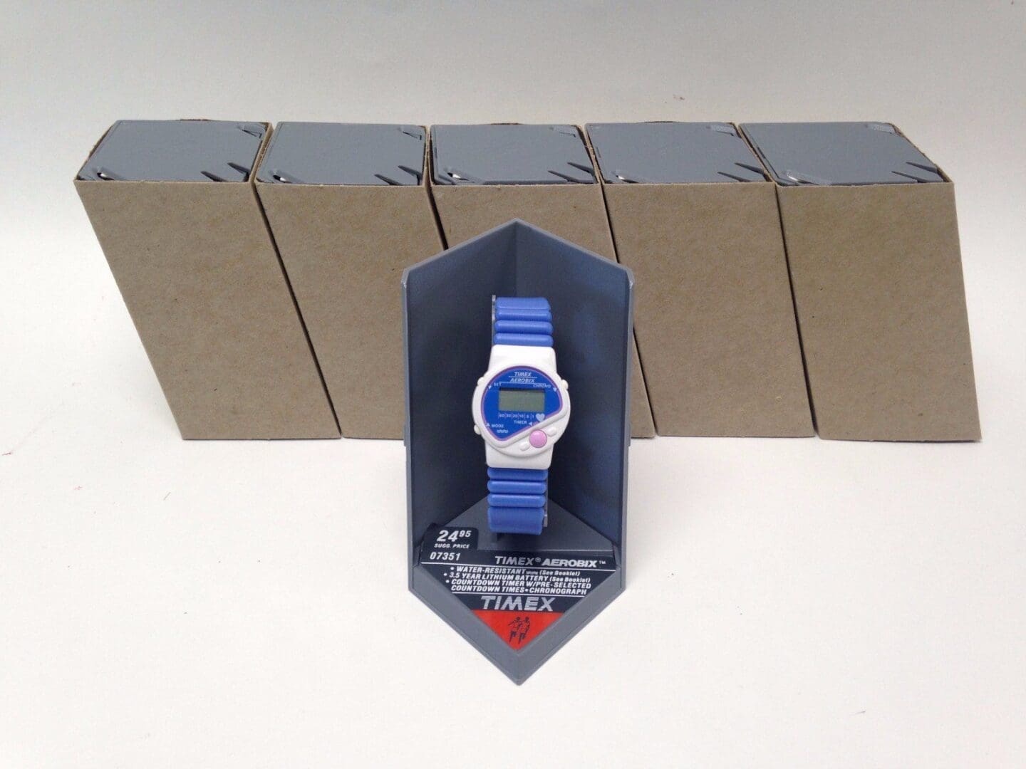 Blue digital watch with packaging boxes behind.