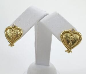 Gold heart-shaped earrings on display stand.