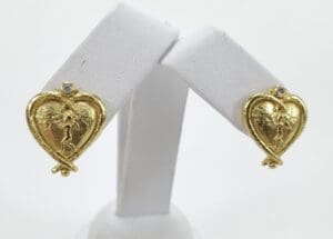 Gold heart-shaped earrings on display stand.
