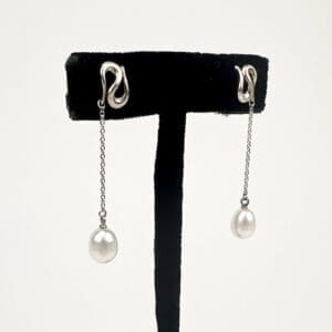 Silver earrings with dangling pearls displayed.