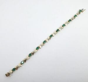 Gold bracelet with green gemstones, white background.