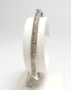 Diamond-encrusted silver bangle on display stand.
