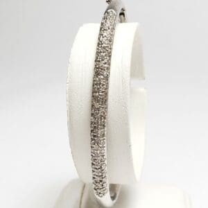Diamond-encrusted silver bangle on display stand.