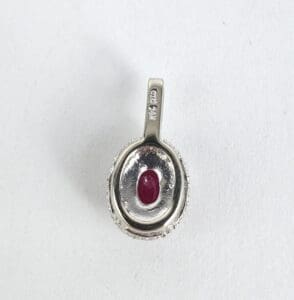 Silver pendant with red gemstone center.