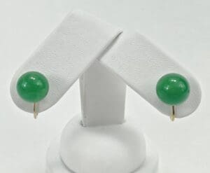 Green gemstone stud earrings on white stand.