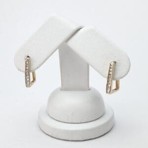 Gold earrings with diamonds on white stand.