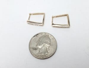 Gold earrings beside a U.S. quarter.