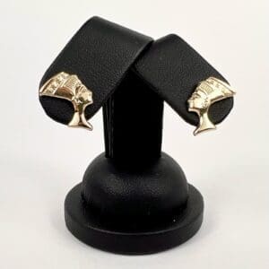 Gold Egyptian-themed cufflinks on black stand.