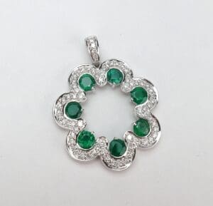 Flower-shaped silver pendant with green stones.