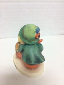 Figurine of child wearing green hat and coat.